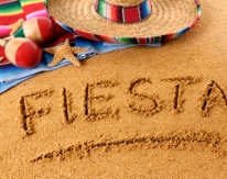 The word Fiesta written on a sandy beach, with sombrero, traditional serape blanket, starfish and maracas (studio shot - warm color and directional light are intentional).