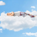 Tranquil scene of a young woman dreaming and sleeping on a cloud up in the sky